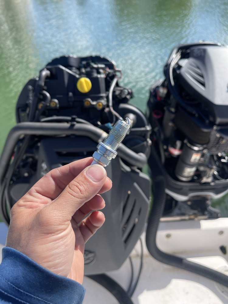 Fresh spark plug held up during a 100-hour outboard service on the water